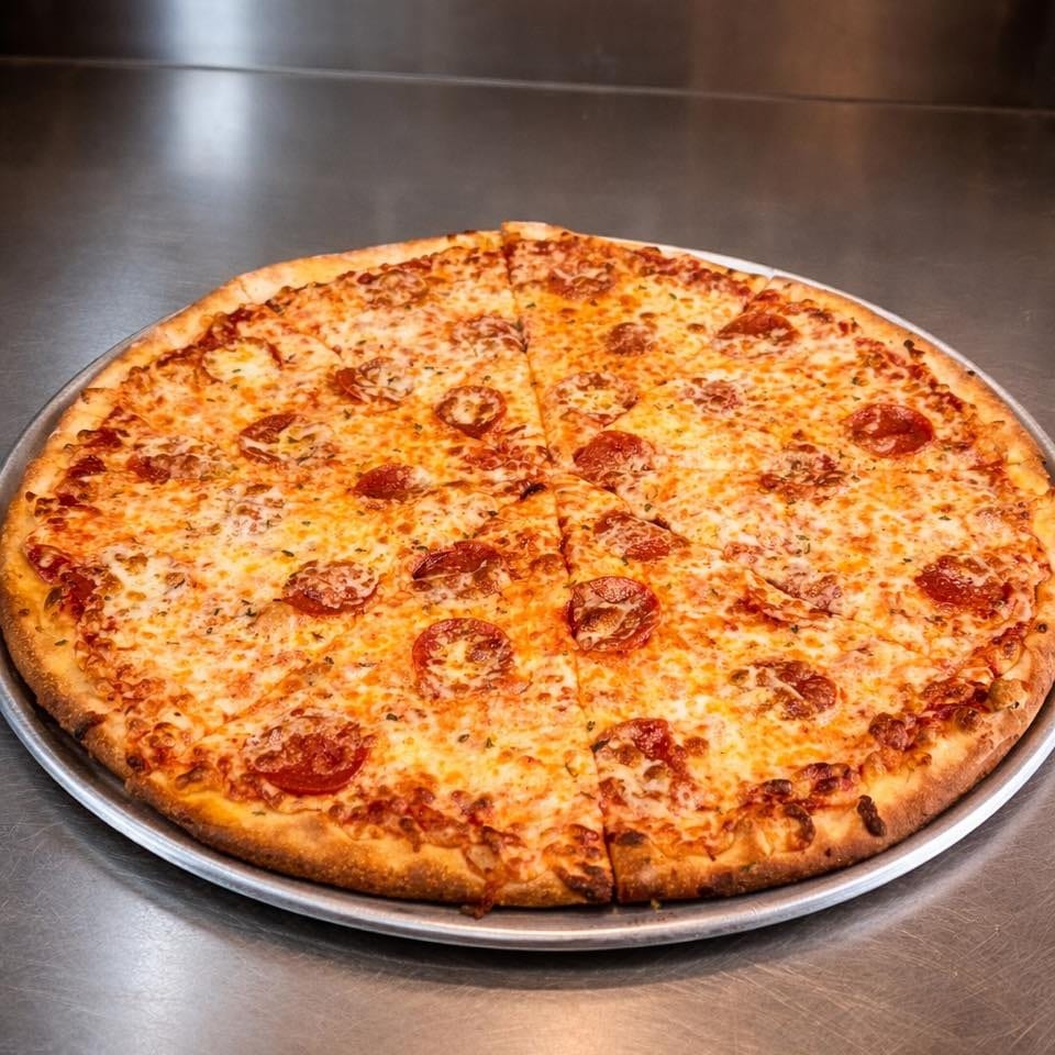 A whole pepperoni pizza, sliced into eight pieces, on a metal tray with a brick wall background.