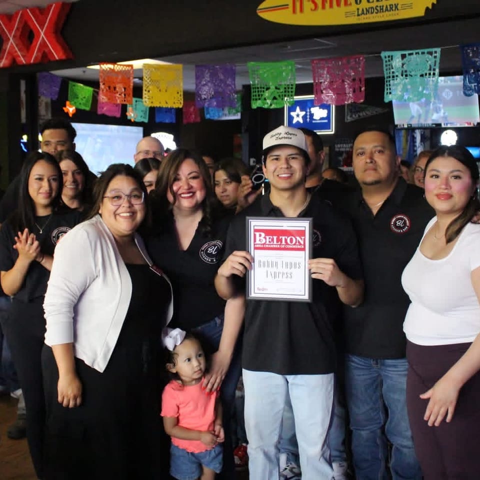 A group of people, including a child, smiling and posing with a "Belton" certificate in a restaurant.