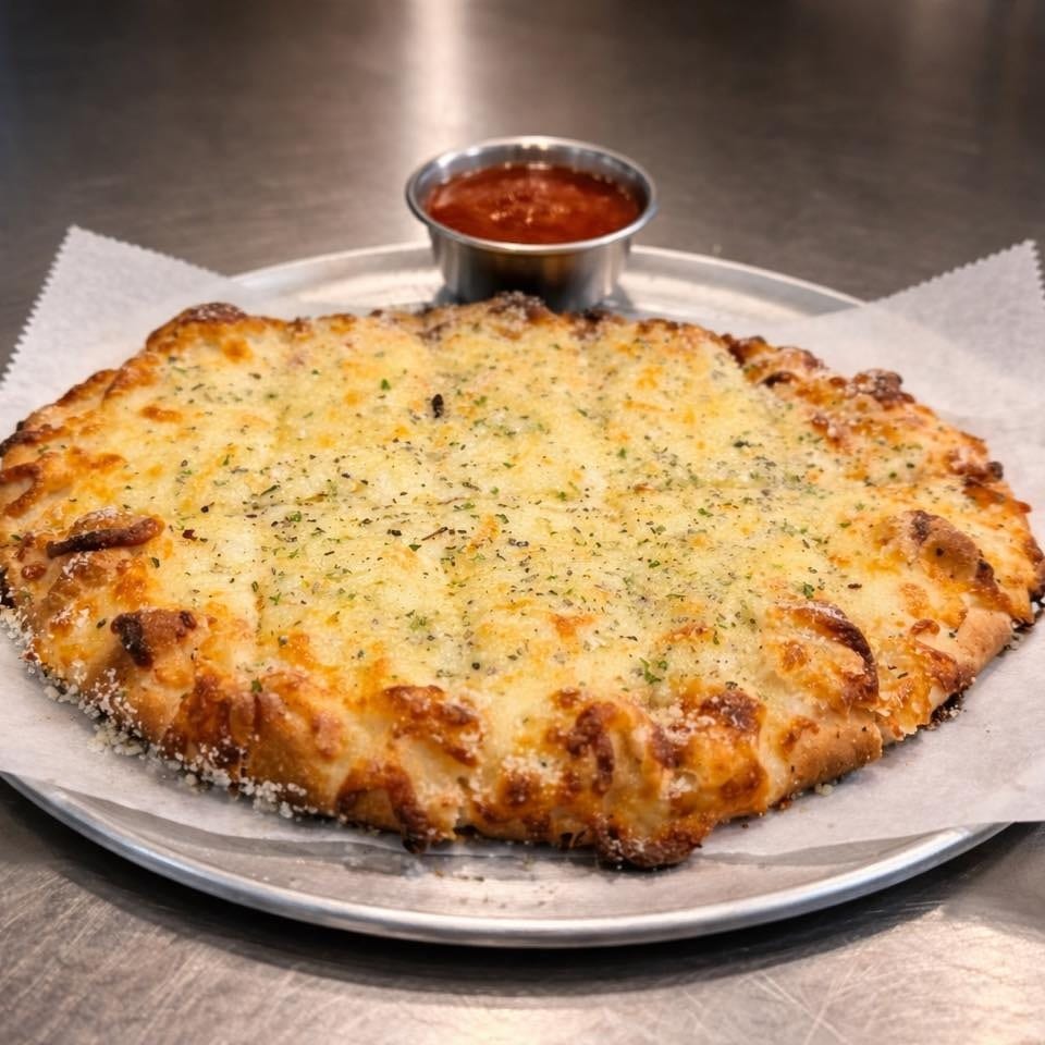 A cheesy garlic bread on a metal plate with a side of marinara sauce.