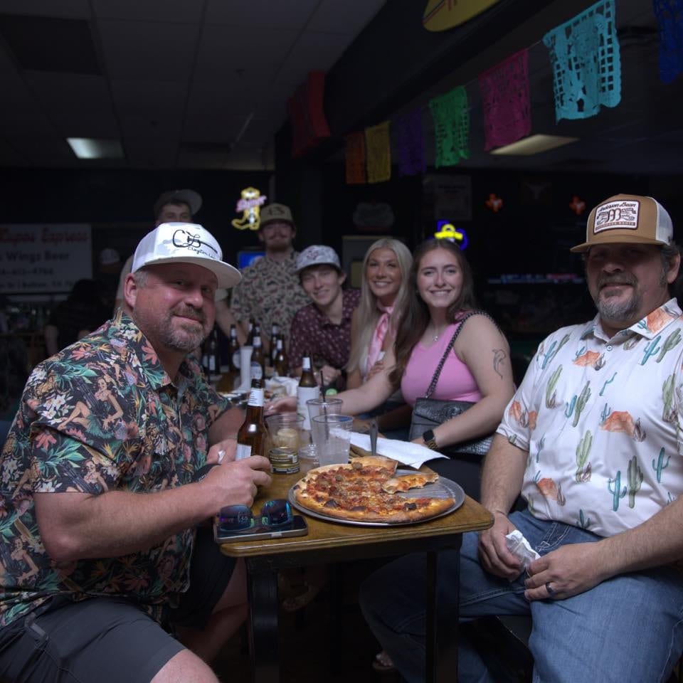 Group of people enjoying pizza and drinks at a dimly lit restaurant with colorful decorations.
