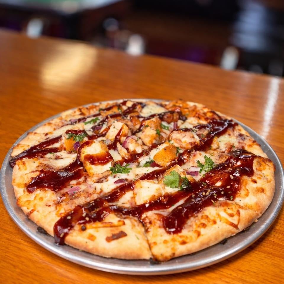 BBQ chicken pizza with red onions and cilantro on a metal tray on a wooden bar.